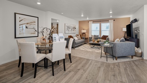 A dining area with a small metal table surrounded by off white chairs, in the background you can see into the living area.