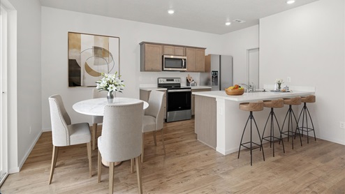 Dining area with a round white table and white dining chairs and kitchen with stainless steel appliances, wood cabinets, and a white island with four brown stools.