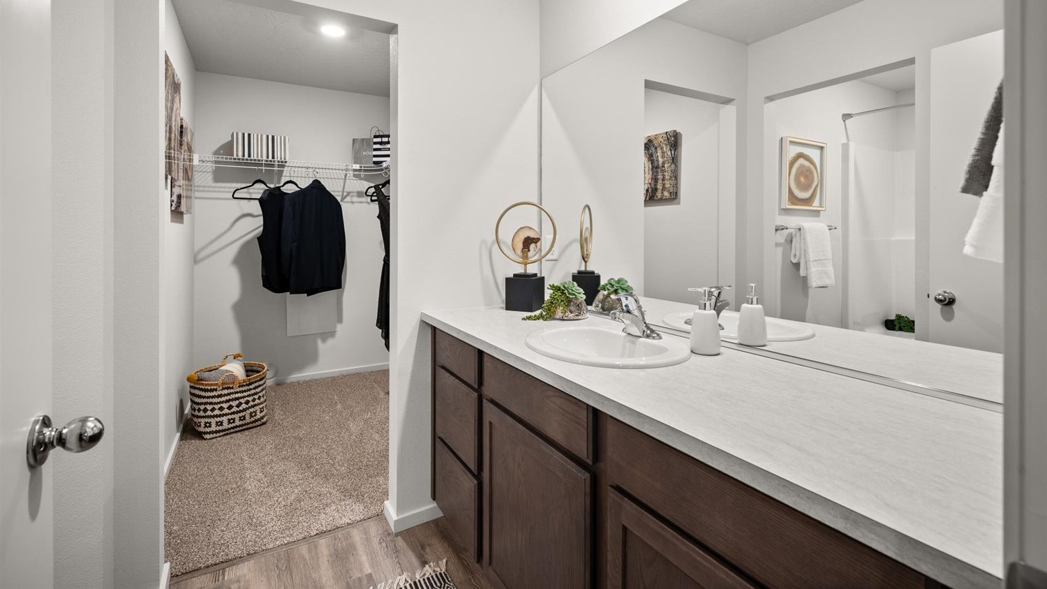 A bathroom with brown wooden cabinets and a white patterned countertop, the door in the back leads to a walk in closet.