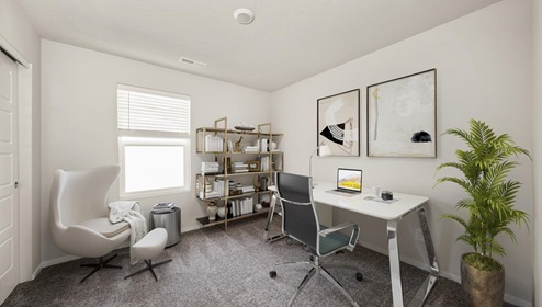 A room with a white office desk and grey chair and two frames hanging above the desk, there's a white accent chair in the left corner and a bookshelf against the back wall next to a window.