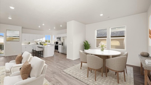 A dining area with a round white table and grey chairs and a view into the kitchen area.