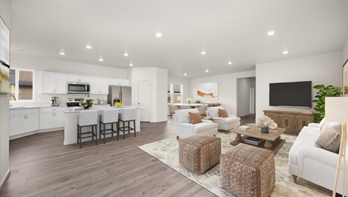 A living area with a light rug, white couch and accent chairs, and a wood coffee table and a kitchen with white cabinets and stainless steel appliances.