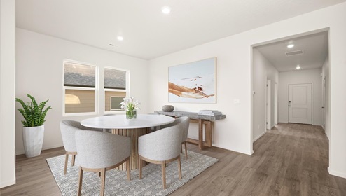A dining area with a round white table and grey chairs and a view into the kitchen area.