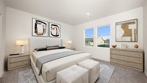 A bedroom with a bed with white sheets and two side tables with lamps. There's a dresser and two large windows.