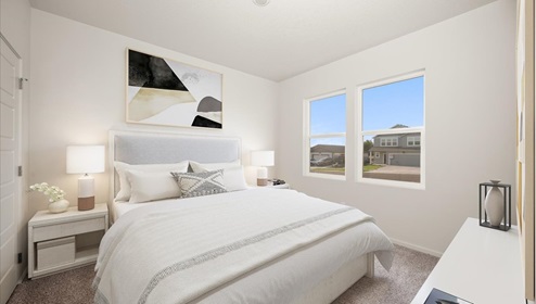 A bedroom with a bed with white sheets and two side tables with lamps. There's a dresser and two large windows.