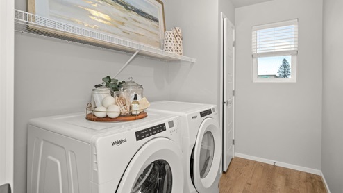 A laundry room with a washer and dryer, a shelf displaying a large painting, and one small window letting in natural light.