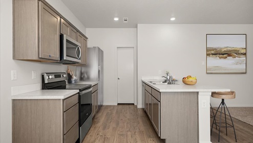 A kitchen with wood cabinets, stainless steel appliances, and a large peninsula with four wooden stools.