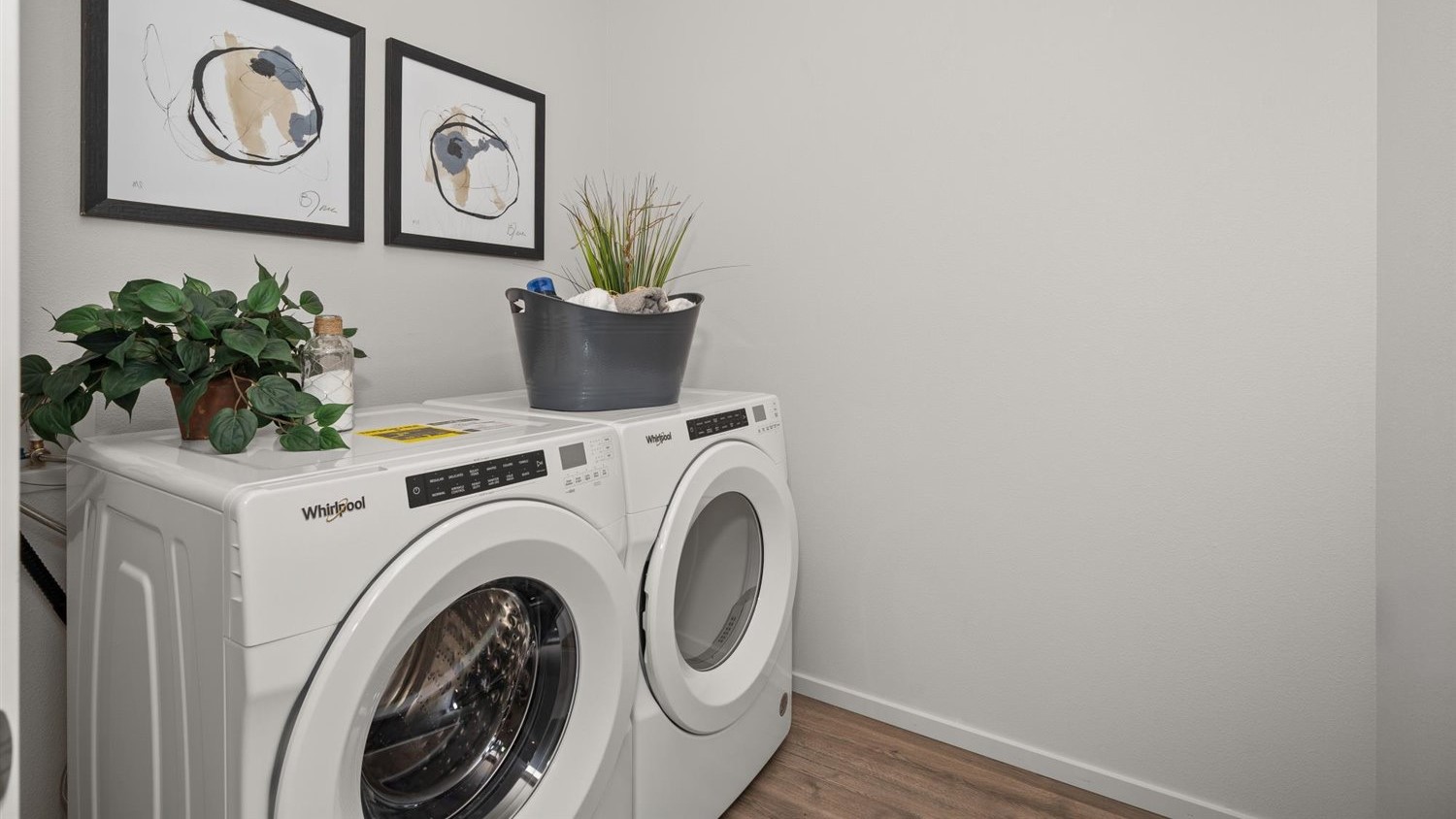 A laundry room with a washer and dryer with plants sitting on top.
