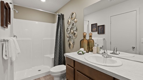 A bathroom with brown wooden cabinets and a light countertop with various decor placed in the corner.