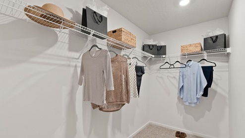 A walk in closet with clothes hanging on wire shelves.