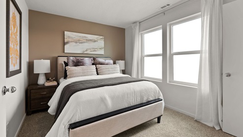 A bedroom with a large bed with white sheets and decorative pillows, two nightstands with lamps, abstract art on the walls, and two large windows letting in natural light.