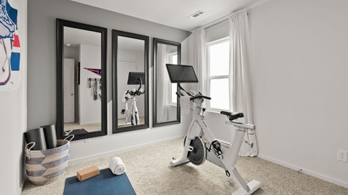 An exercise room with an elliptical bike and three large mirrors and one large window letting in natural light.