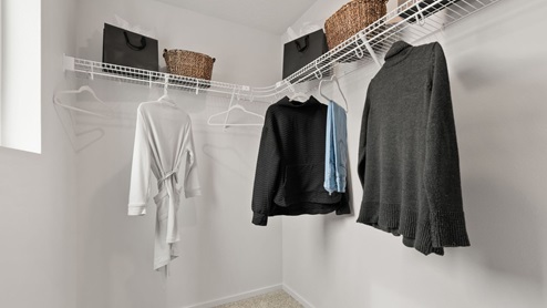 A walk in closet with clothes hanging on wire shelves.