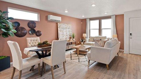 A living area with a black and white patterned rug, white furniture, a wooden coffee table, various decor including lamps and plants, and two large windows letting in natural light framed by white curtains.