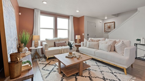 A living area with a black and white patterned rug, white furniture, a wooden coffee table, various decor including lamps and plants, and two large windows letting in natural light framed by white curtains.