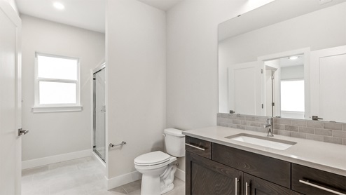 Three-quarter bathroom with step-in shower and doors to hall and secondary bedroom on main floor of Windom plan