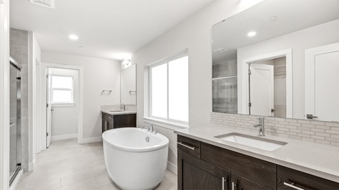 Primary en suite bathroom with two vanities, standalone tub, glass front step-in shower, and private water closet