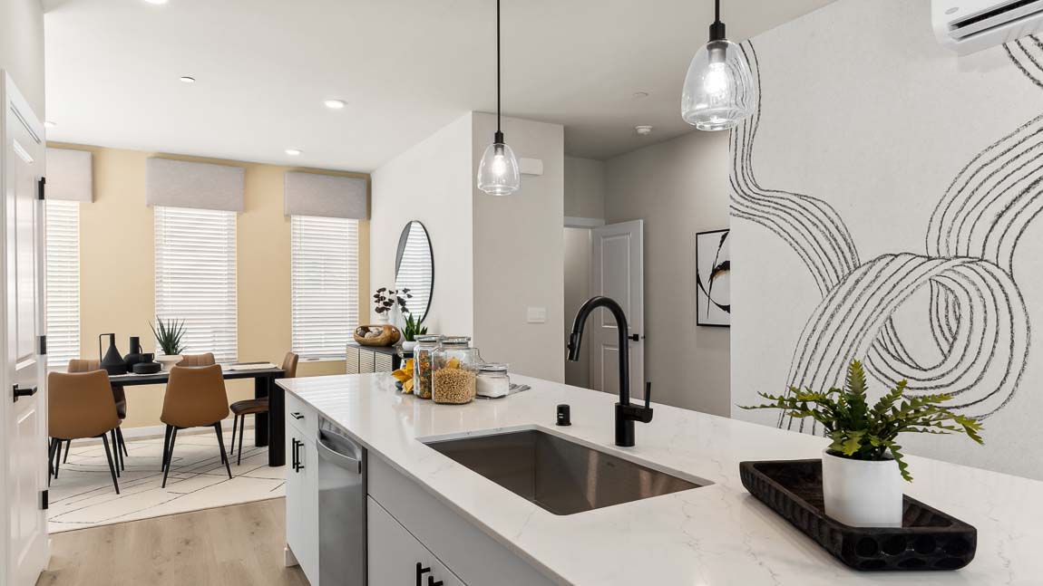 Stainless steel kitchen appliances shown with quartz countertops and dining room in background