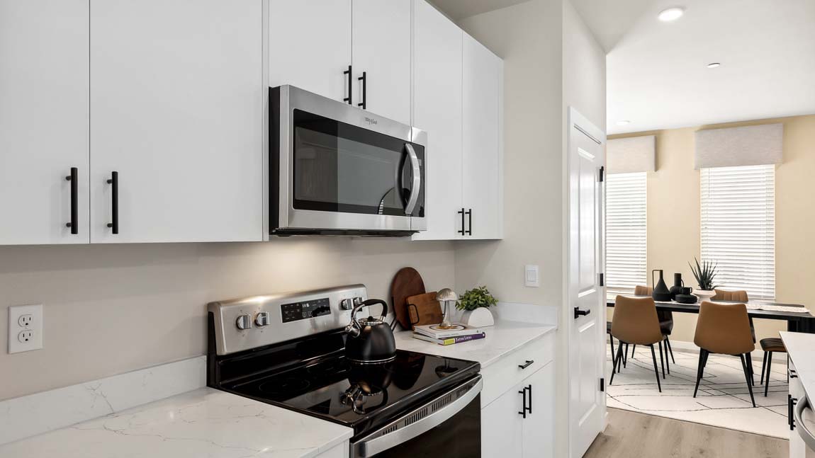 Stainless steel kitchen appliances shown with quartz countertops and dining room in background