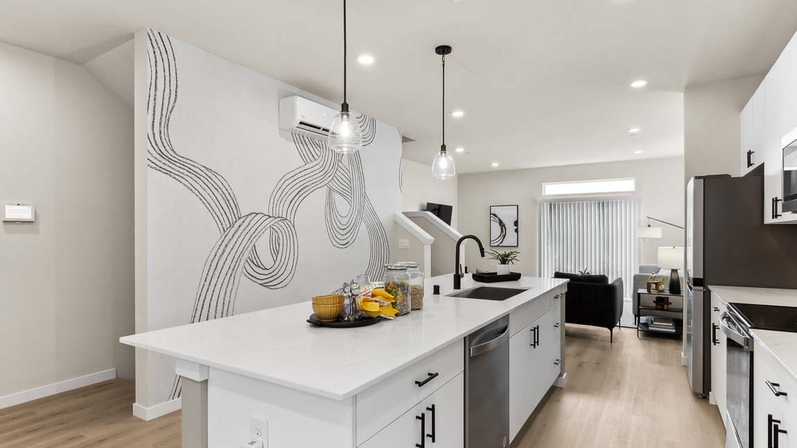 Behind an expansive kitchen island at Cathcart Crossing model home with wall artwork and living room in background