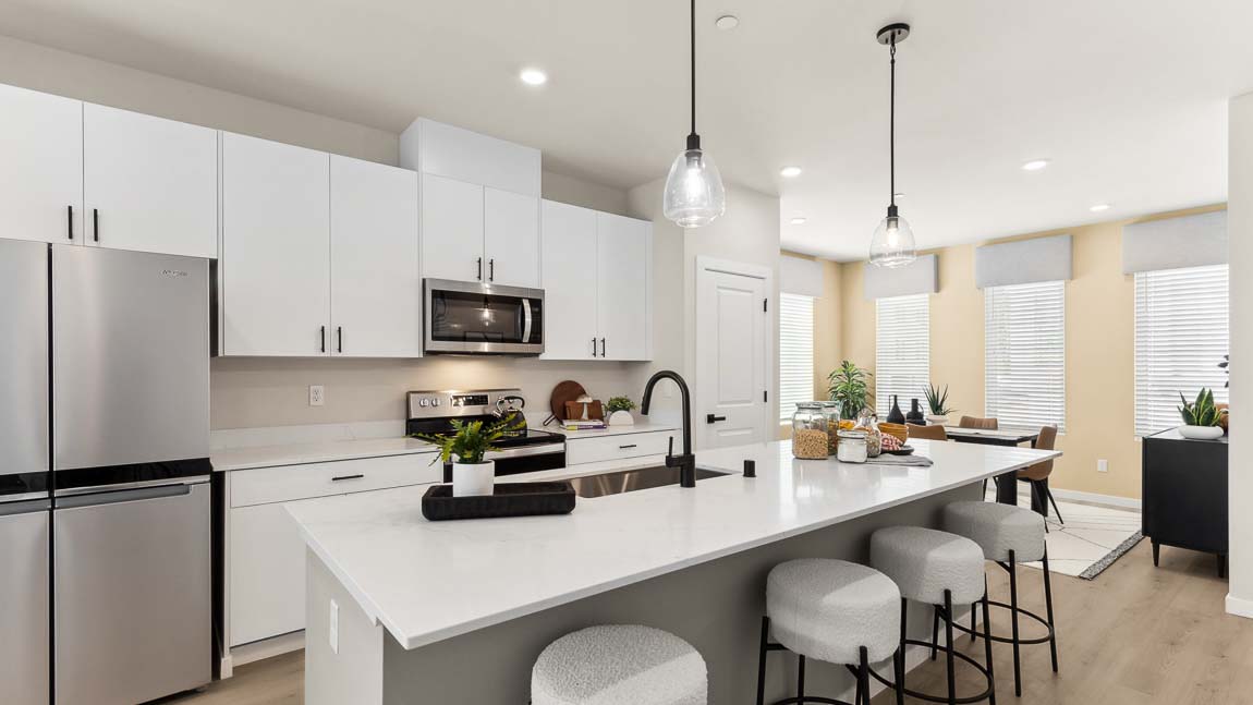 Expansive island in this model home kitchen with white cabinetry, stainless steel appliances, and pendant lighting
