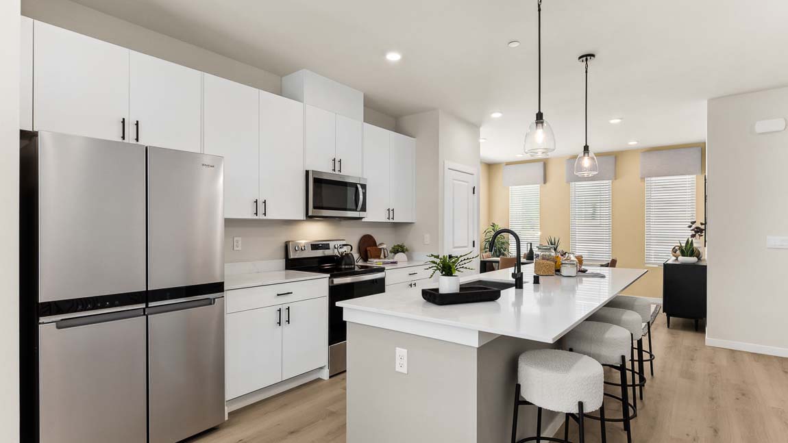 Full view of entire Addison model home kitchen with large center island, stainless steel appliances, with dining room in background