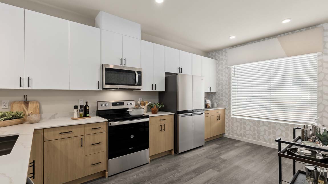 Bennett model home kitchen features a bright window, dual-color cabinetry, stainless steel appliances, and quartz countertops