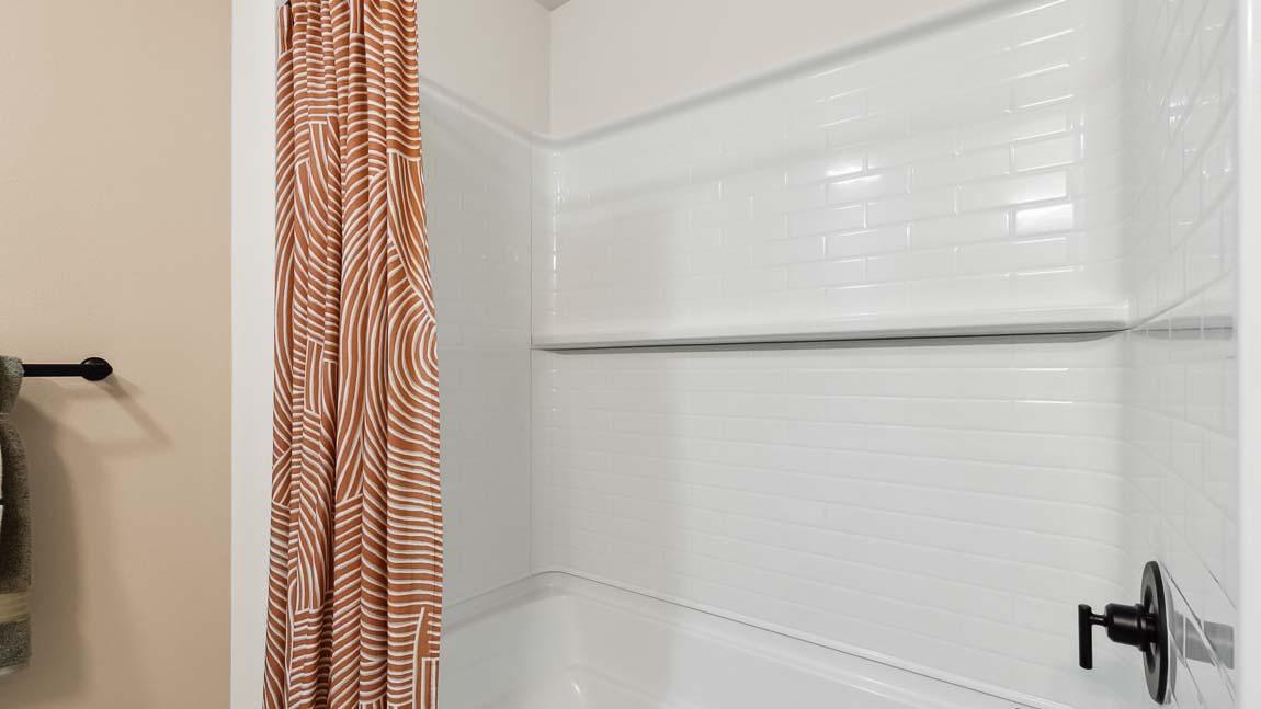 Hallway bathroom tub-shower combo in Bennett model home that includes a built-in shelf
