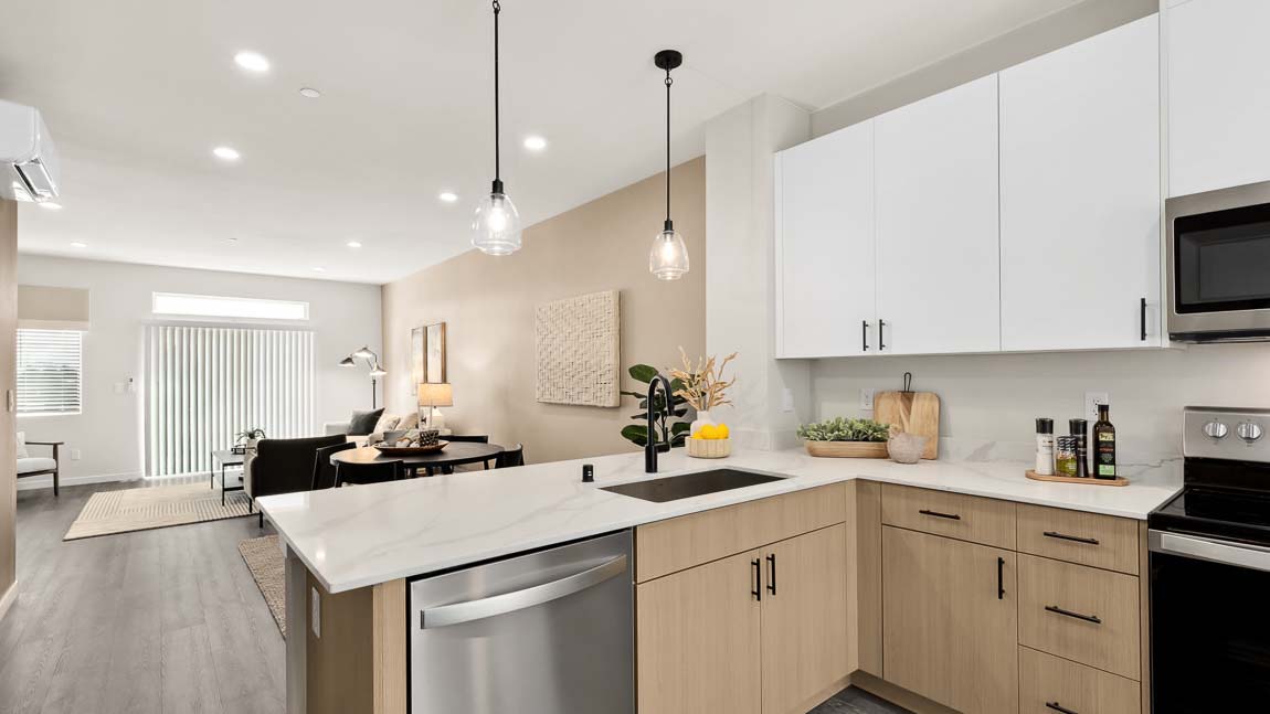 Model home kitchen peninsula with two pendant lights above, with dining and living spaces in background