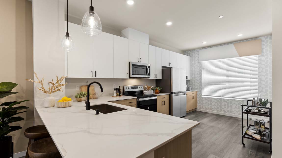 View of expansive kitchen peninsula with pendant lighting, dual-color cabinetry, and stainless-steel appliances in Bennett model home