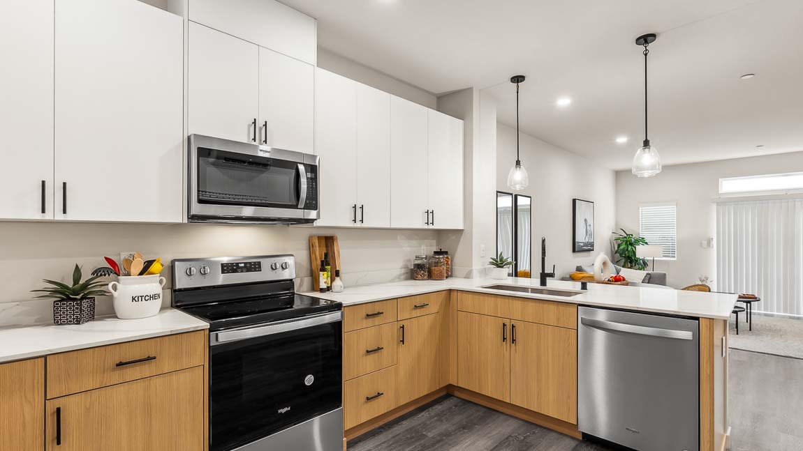 Alternate view of Capri model home kitchen with dual-color cabinetry, stainless steel appliances including dishwasher, and peninsula with pendant lighting
