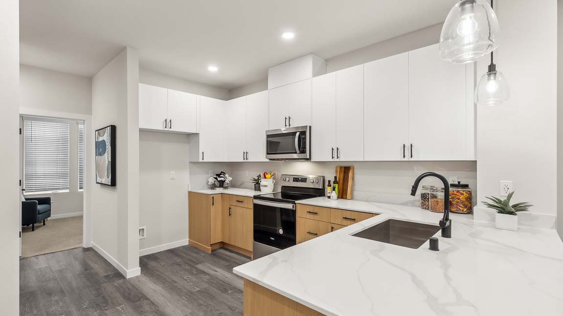 Alternate wide-angle view of Capri model home kitchen peninsula featuring quartz countertops and pendant lighting above