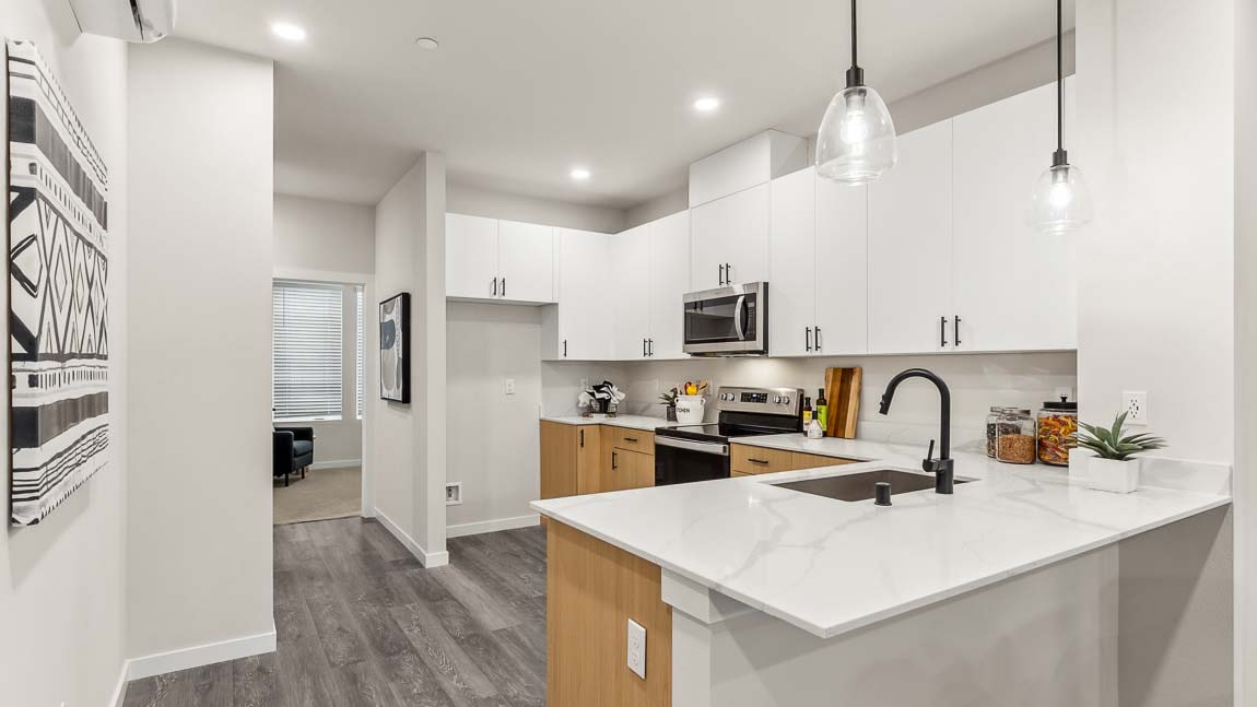Light and bright model home kitchen with dual-color cabinetry, and peninsula with pendant lighting above