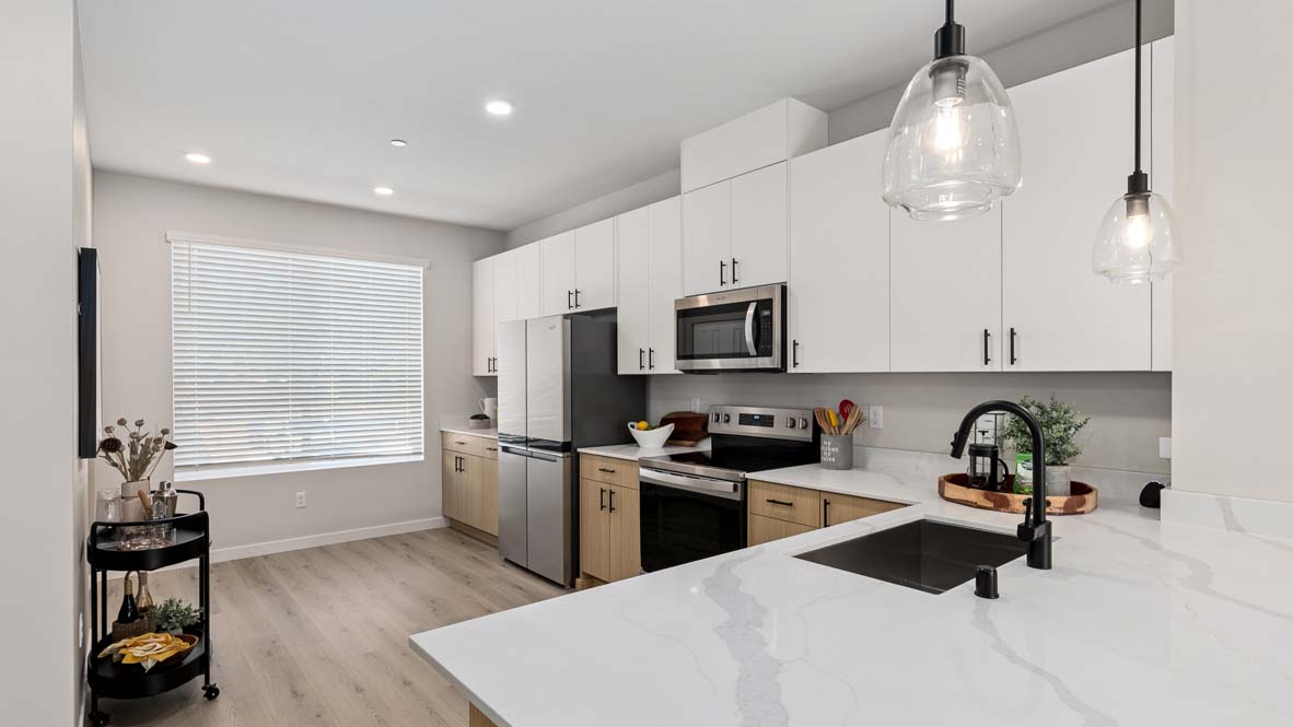 Stainless steel appliances featured in model home kitchen with dual-color cabinetry, and peninsula
