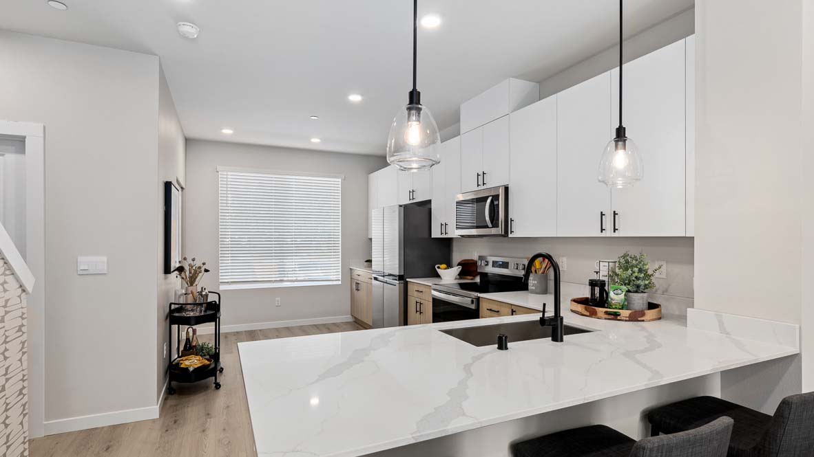 Model home kitchen peninsula with two pendant lights above, with dining and living spaces in background
