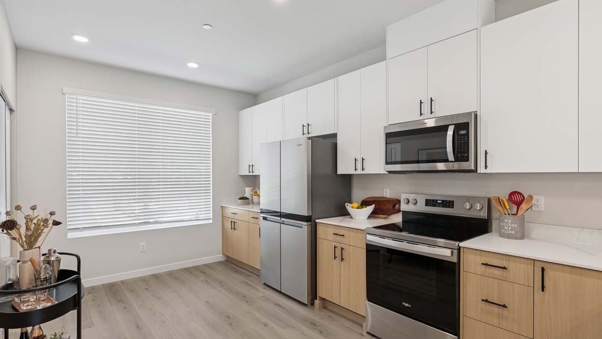 Model home kitchen peninsula with two pendant lights above, with dining and living spaces in background