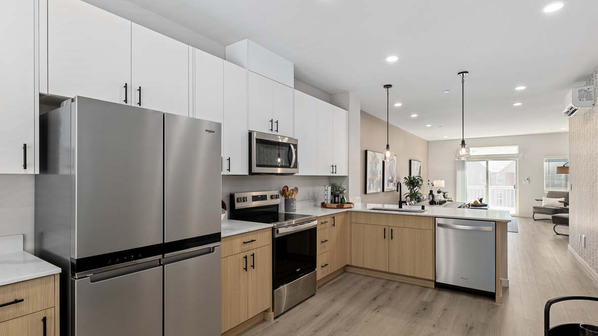 View of expansive kitchen peninsula with pendant lighting, dual-color cabinetry, and stainless-steel appliances in Bennett model home