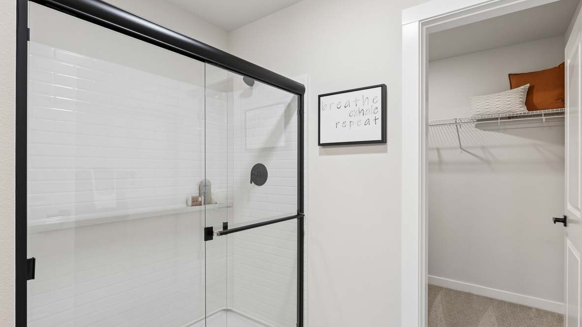 Close up of private bathroom step-in shower with double-door glass enclosure and built-in shelf, with nearby walk-in closet