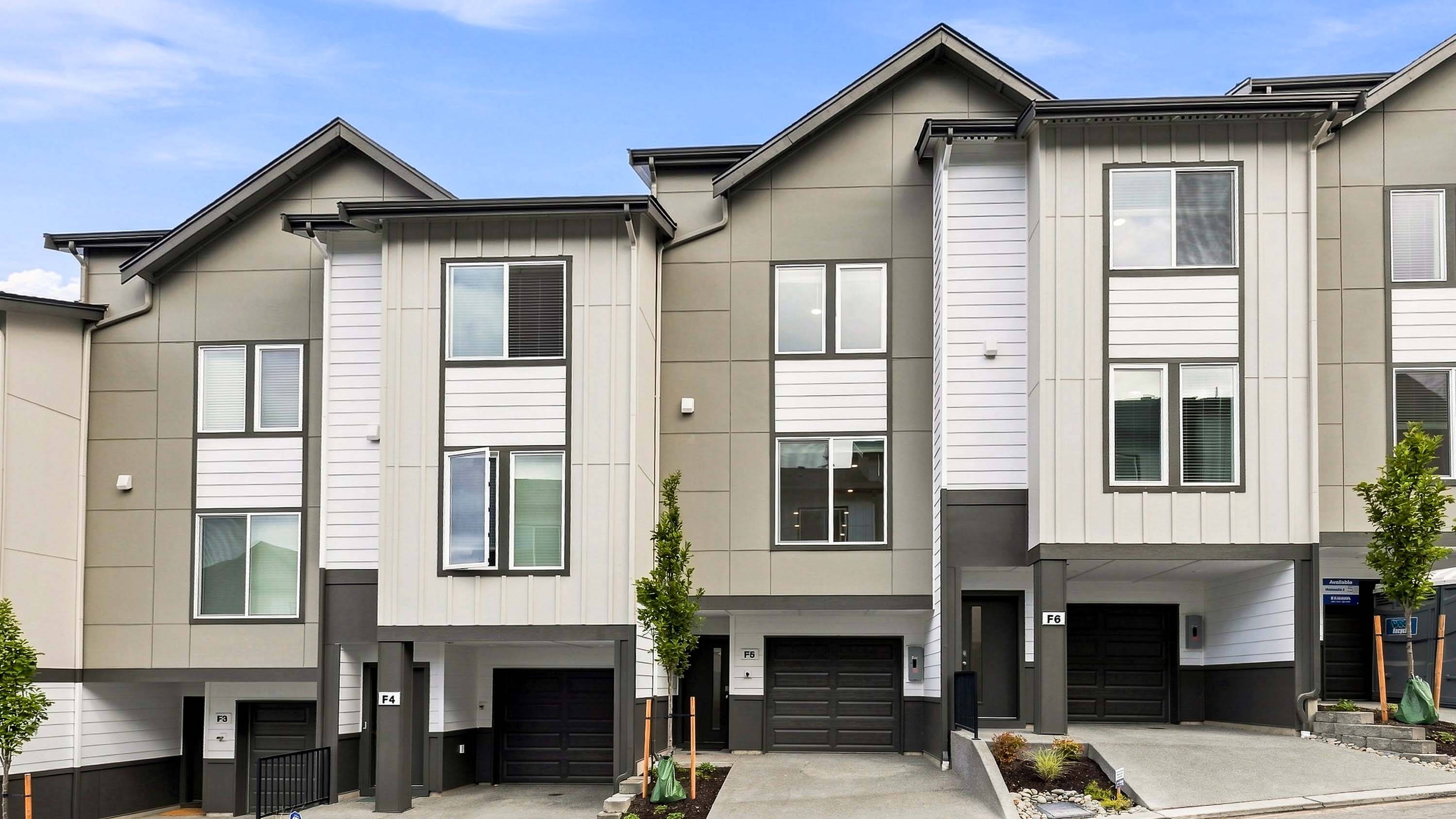 Exterior view of modern three-story townhomes with attached garages, contemporary siding, landscaped entryways, and paved driveways.