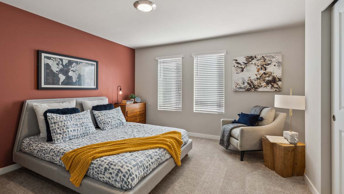 Spacious bedroom with upholstered bed, accent wall, large windows, cozy seating area, and neutral-toned furnishings.