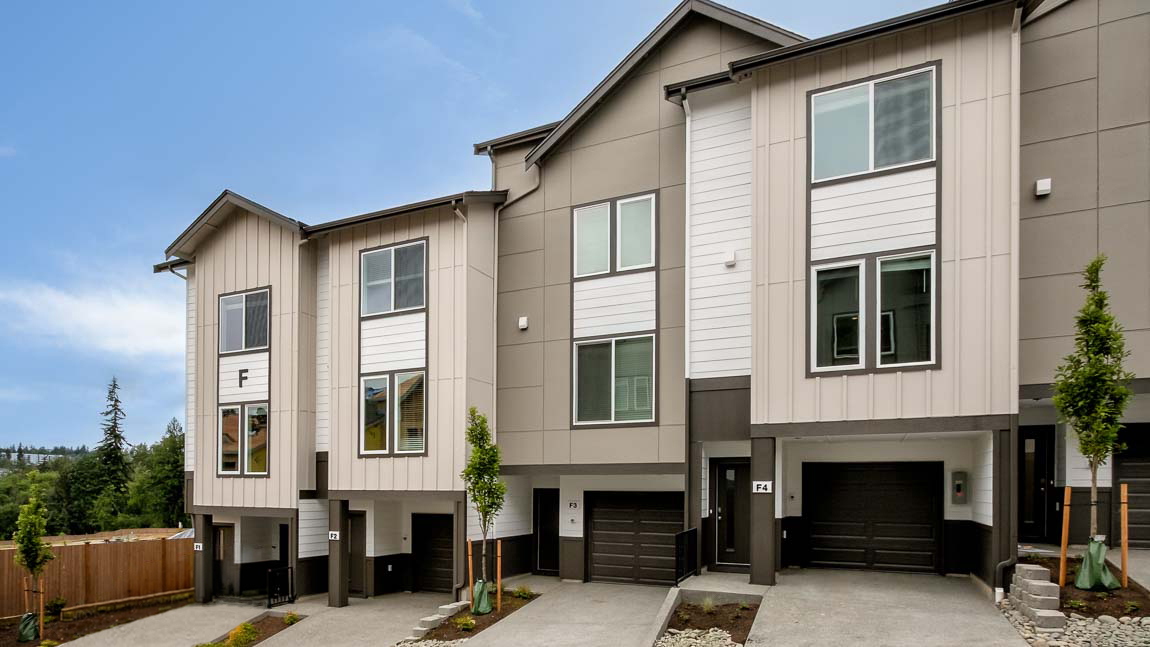 Exterior view of modern three-story townhomes featuring attached garages, contemporary architecture, and landscaped front walkways.