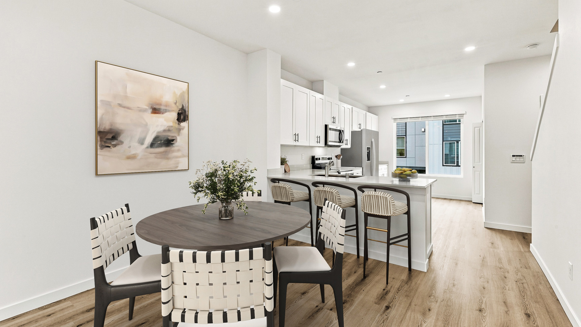 Open dining and kitchen area featuring a round dining table, four chairs, breakfast bar seating, white cabinetry, and wood-look flooring.