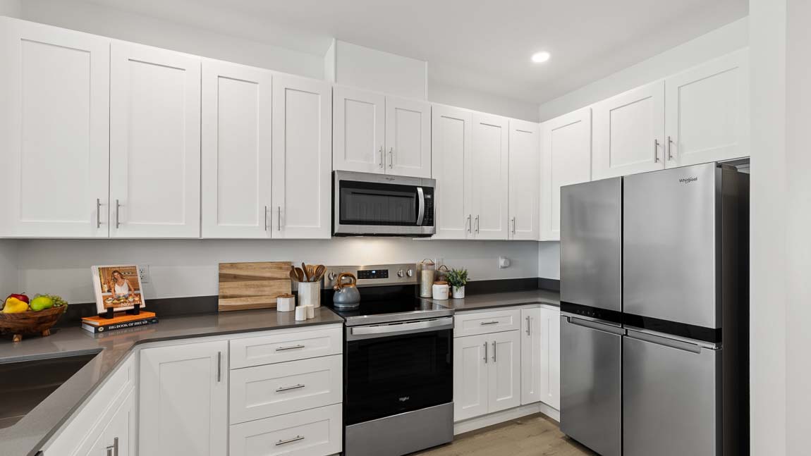 Modern kitchen with abundant white cabinetry, stainless steel refrigerator, electric range, microwave, and gray countertops.