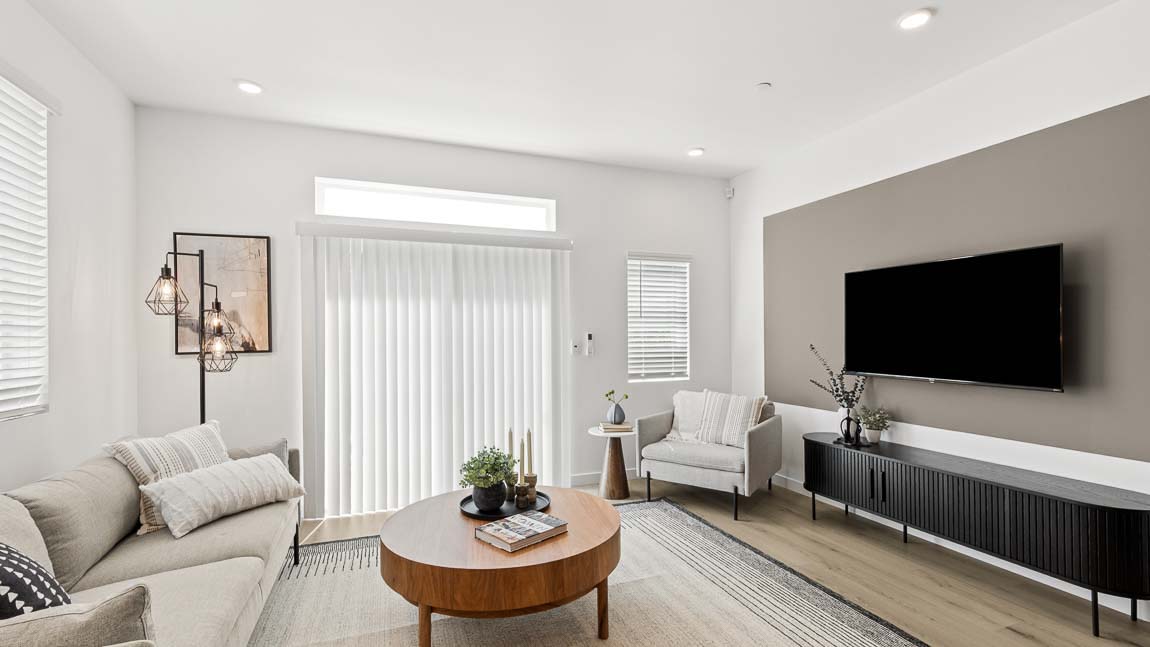 Comfortable living room with sofa, accent chair, large wall-mounted television, coffee table, and sliding glass door access.
