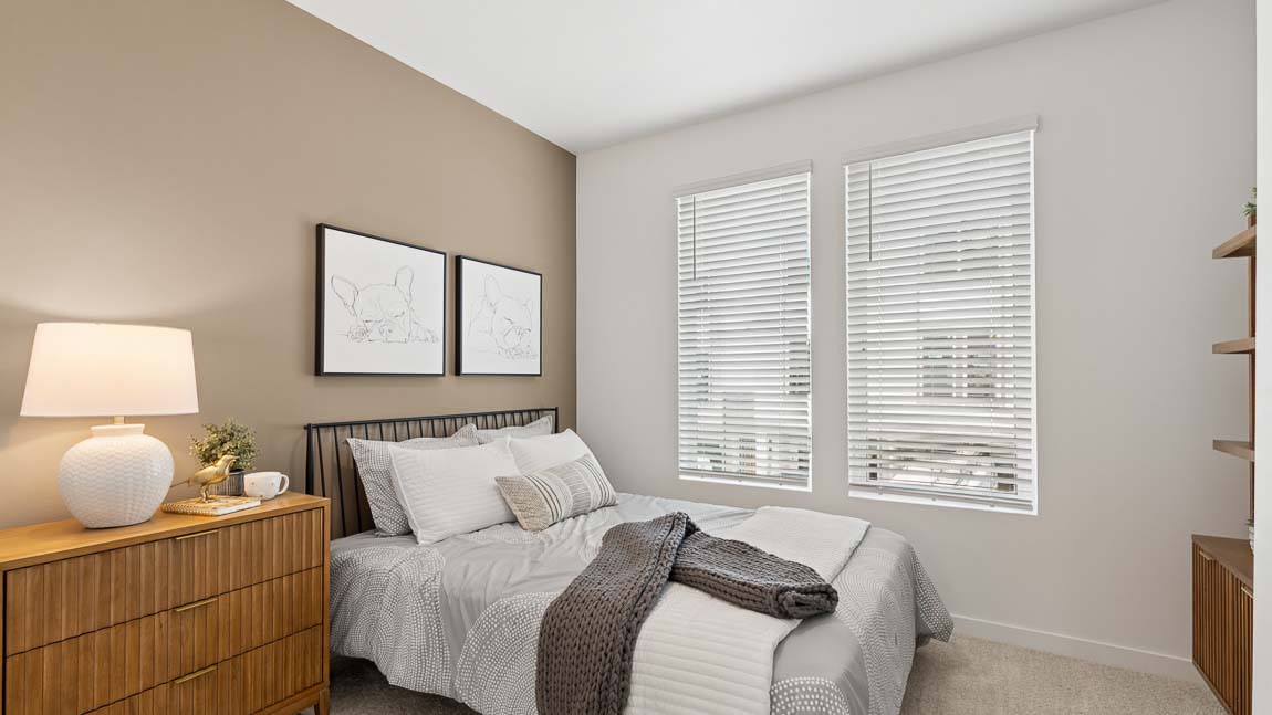 Secondary bedroom with neutral décor, large windows, upholstered bedding, wood furniture, and soft carpeting.