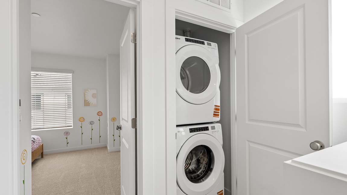 In-home laundry area with stacked washer and dryer located adjacent to a bedroom and hallway storage space.