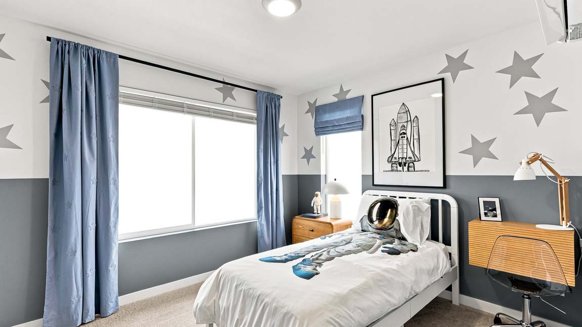Space-themed bedroom with star-patterned walls, a single bed with astronaut bedding, blue curtains, rocket artwork, wood nightstands, and a compact desk.
