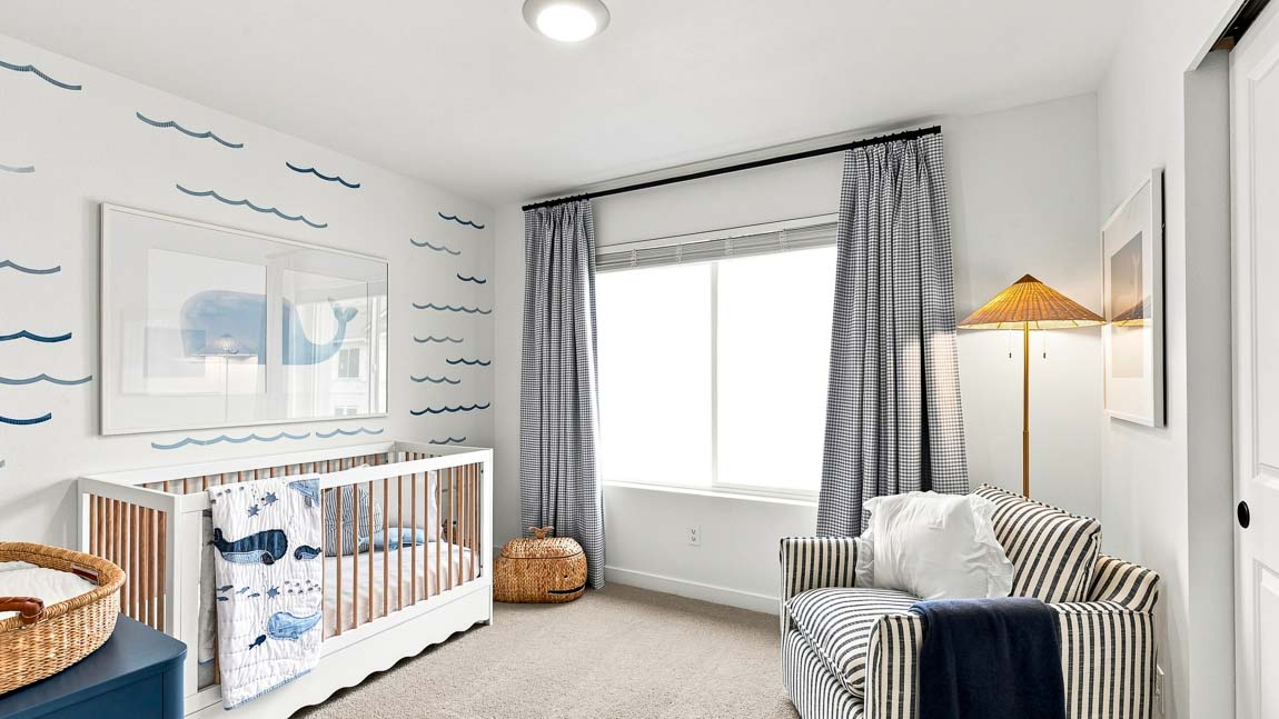 Nursery with a white crib and whale-patterned bedding, blue wave wall decals, striped armchair, woven basket, floor lamp, and black-and-white curtains.