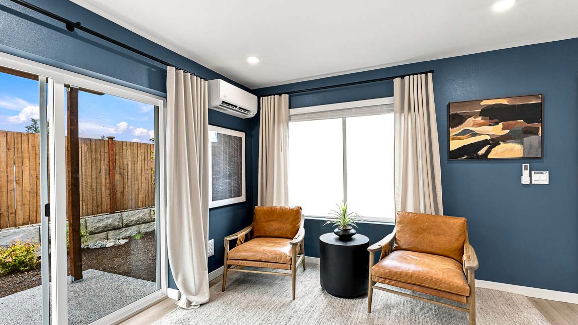 Dining area with a wood table set for six, upholstered chairs, a dark blue accent wall, three tall windows, and beige curtains beside a large window.