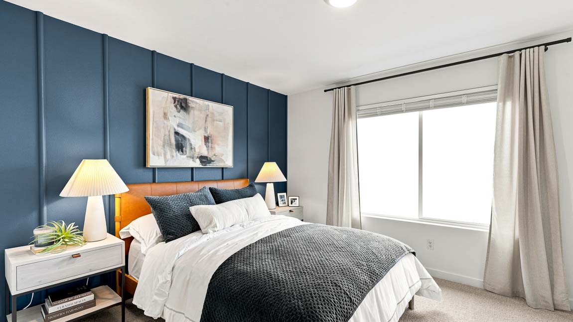 Bedroom with a white bed, dark textured bedding, light nightstands and lamps, an orange upholstered headboard, and a dark blue paneled accent wall.